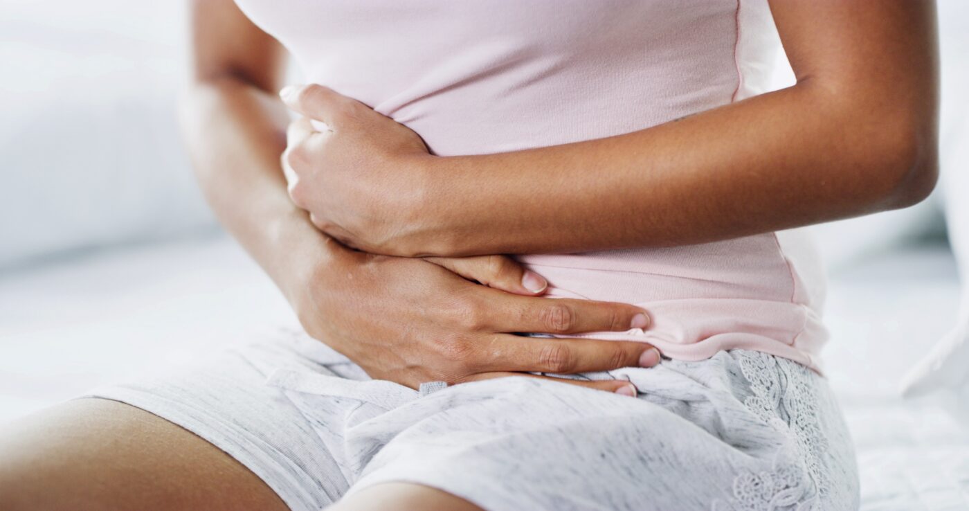 Frau in rosa Top und grauen Shorts hält sich den Bauch mit beiden Händen.