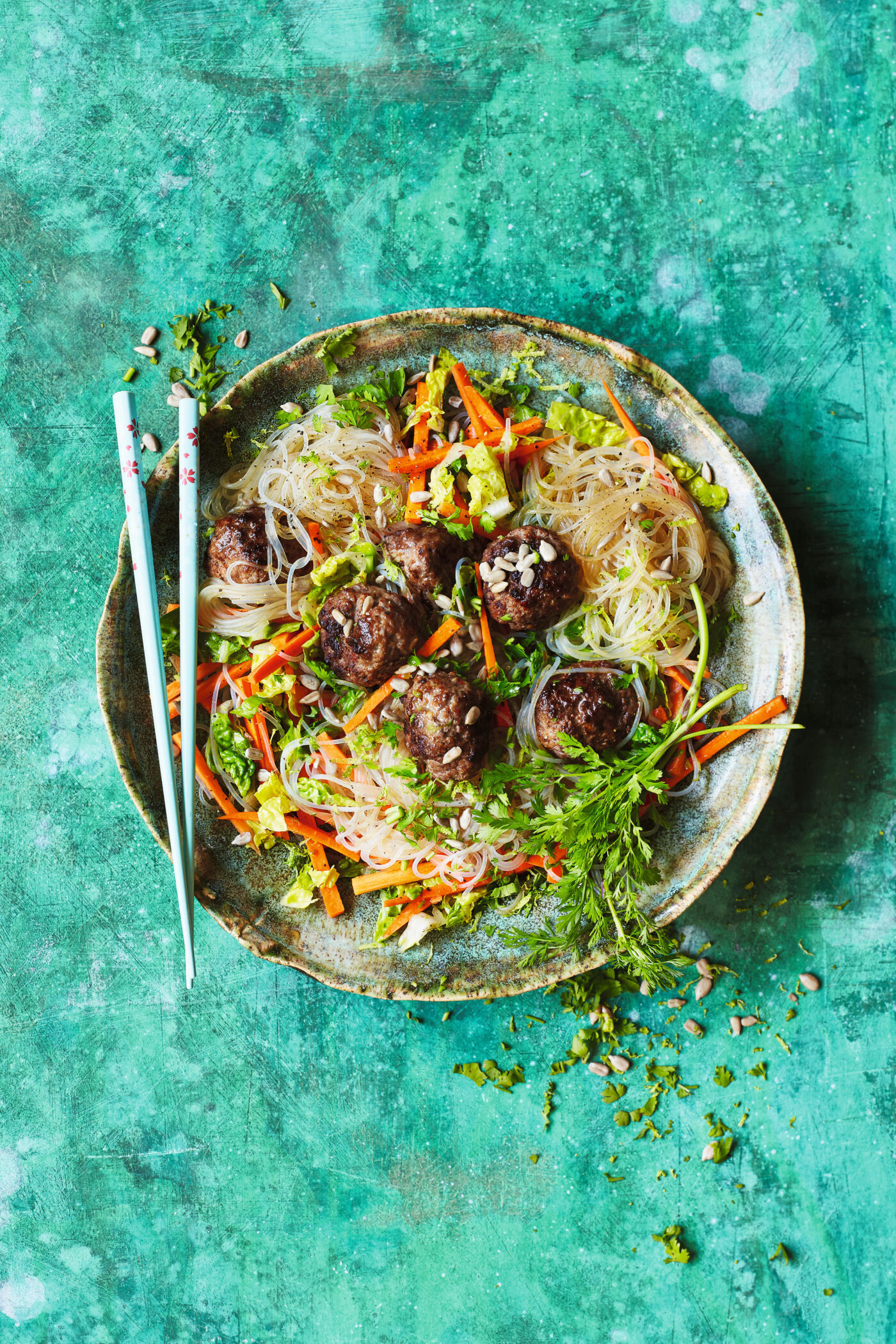 Asiatischer Nudelsalat mit Gemüse und gebratenen Hackbällchen in einer Schüssel, garniert mit frischen Kräutern.