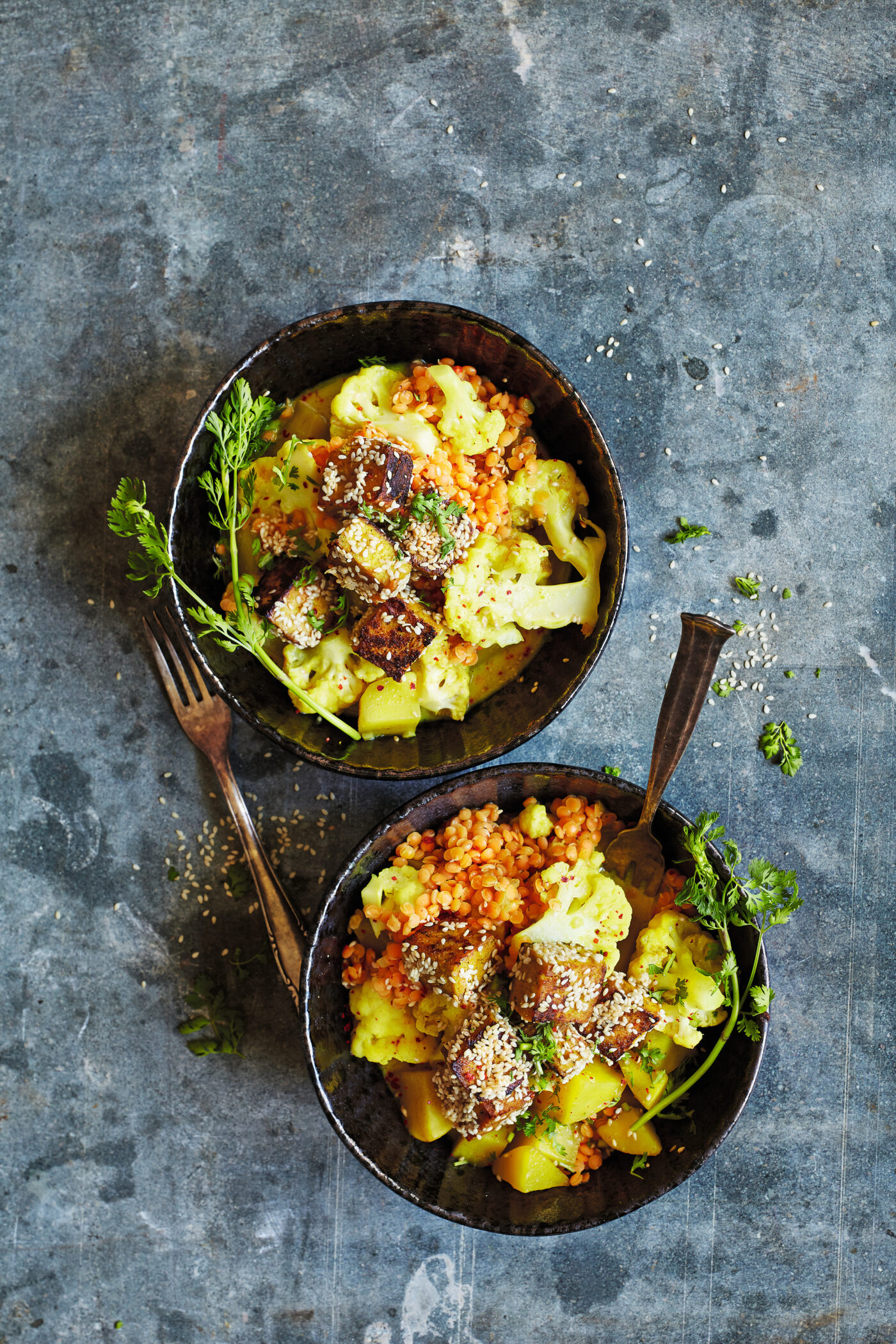 Cremiges Blumenkohl-Kartoffelcurry mit roten Linsen und Tofuwürfeln, serviert in einer Schale mit sichtbaren Gewürzen und Kräutern.