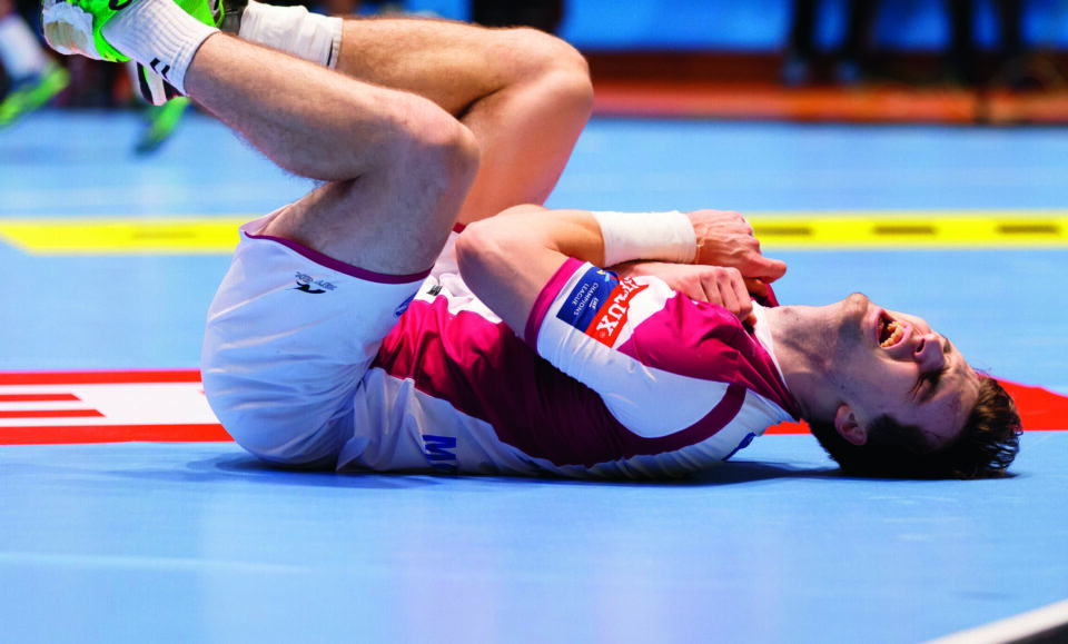 Handballspieler liegt verletzt vor Schmerzen auf dem Spielfeld